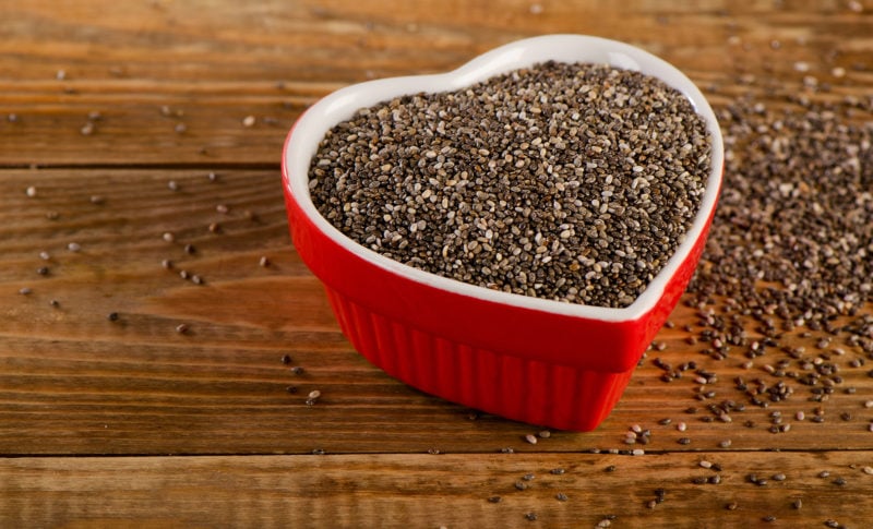 chia seeds inside red heart-shaped bowl over wooden background