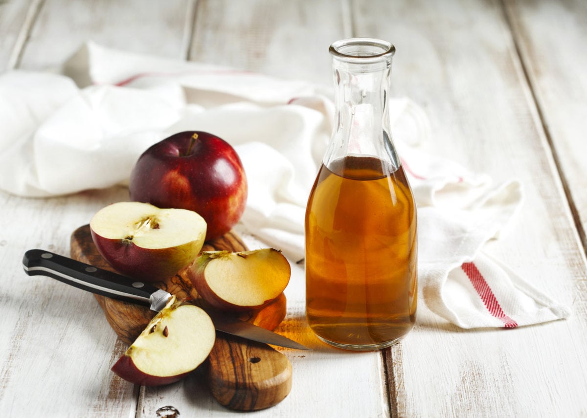 apple cider vinegar with sliced apples on wooden cutting board