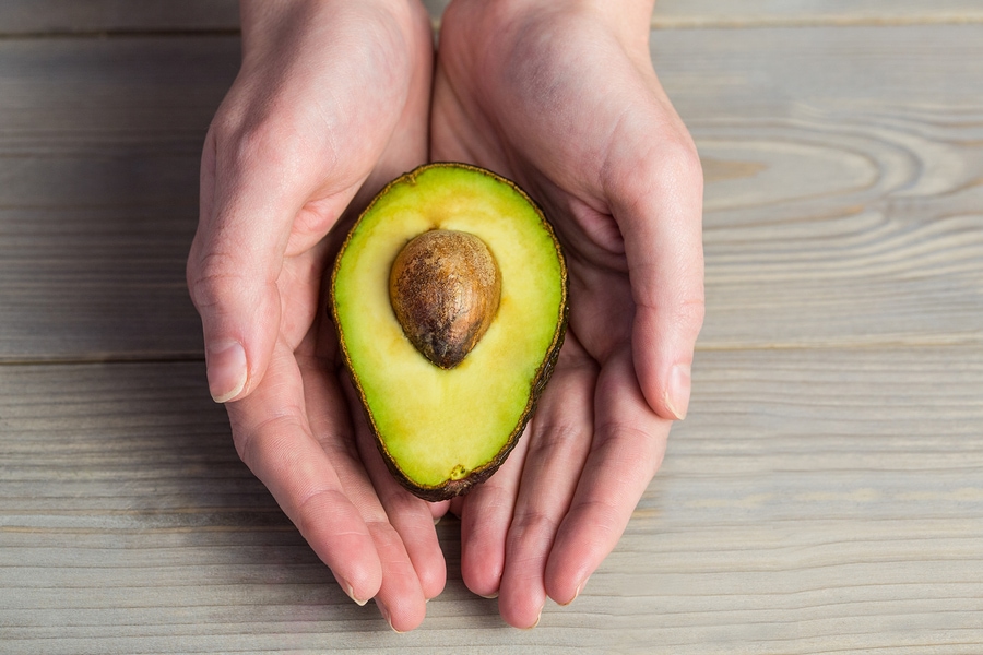 Woman holding sliced avocado with both hands