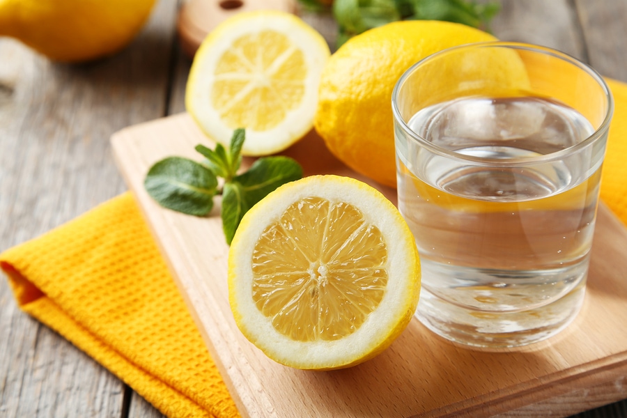 Lemons On Cutting Board With Glass Of Water On Grey Wooden Backg