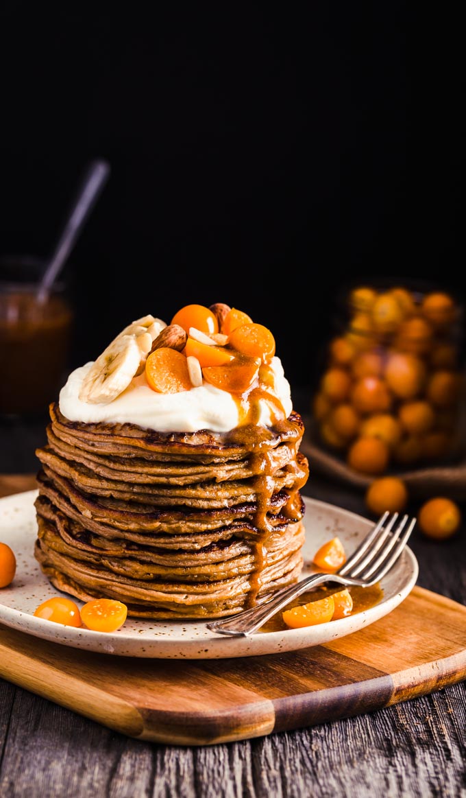 A stack of pancakes with whipped cream and fruits on top.