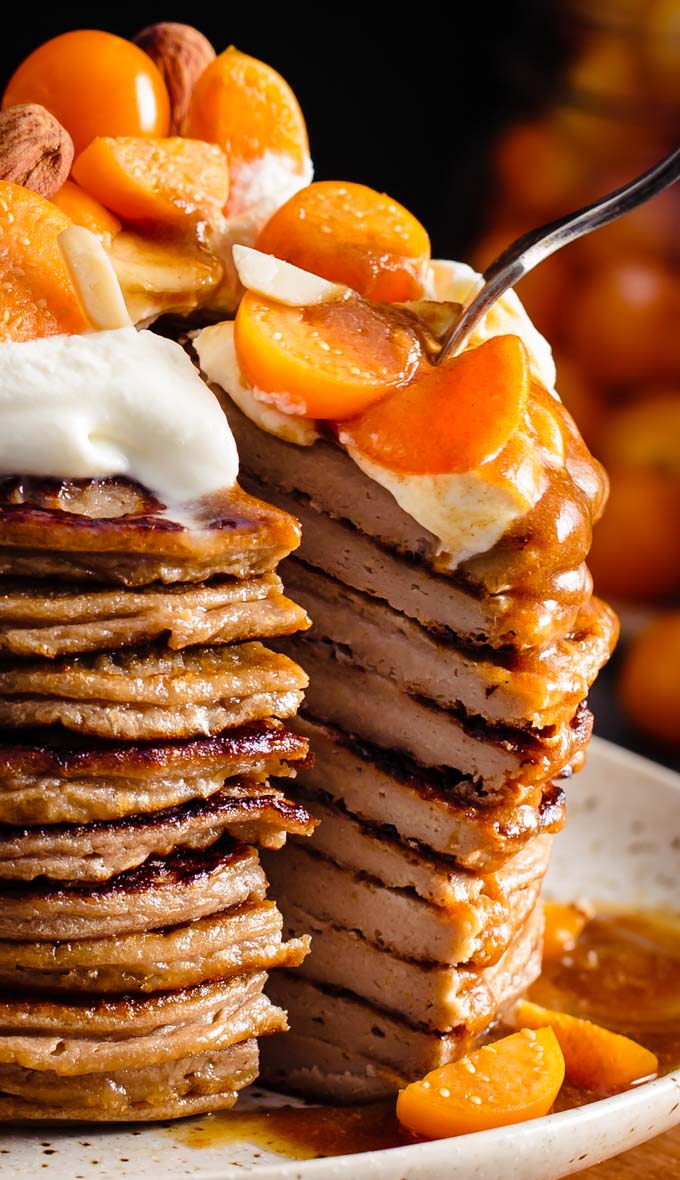 A stack of pancakes with whipped cream and fruits on top. A triangle slice is cut out of the stack and pulled out a bit.