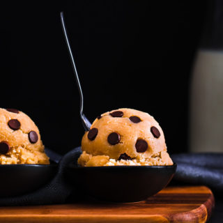 2 Edible cookie dough balls on a wooden board.